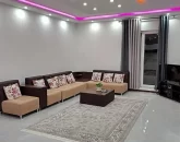 مبلمان قهوه ای رنگ و تلویزیون و سقف نور پردازی شده با نور بنفش سالن نشیمن ویلا در جویبار