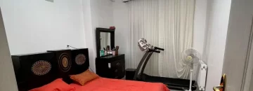 تخت خواب با روتختی قرمز و تردمیل و پنکه و میزآرایش در اتاق خواب آپارتمان در زاغمرز