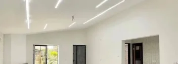 پنجره رو به محوطه وسقف نورپردازی شده با نور سفید و شومینه سالن نشیمن ویلا در خزرآباد