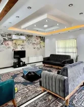 مبلمان طوسی و سبزآبی رنگ و سقف نورپردازی شده با نور زرد و سفید سالن نشیمن ویلا در طاهرآباد