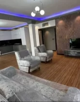 مبلمان راحتی سفید با میز تلویزیون مشکی در سالن نشیمن نور پردازی شده با نور آبی ویلا در نکا